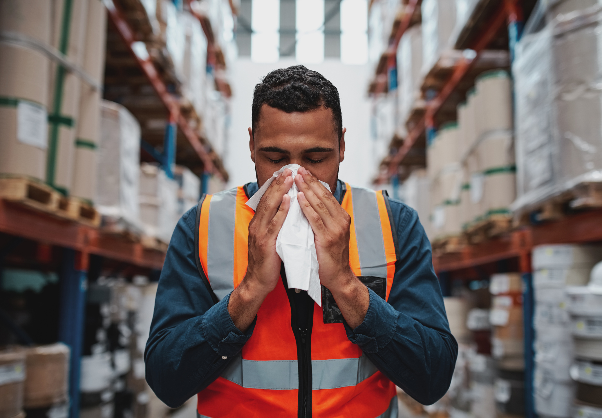 Warehouse worker blowing nose while working wearing safety vest