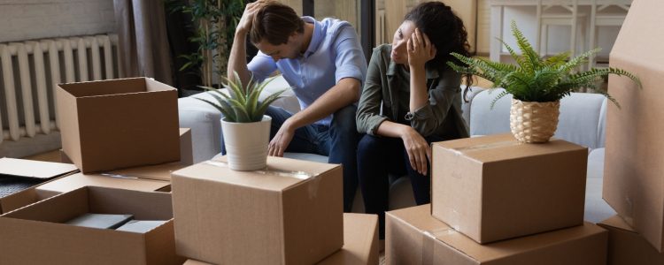 Unhappy frustrated couple sitting on couch with cardboard boxes, eviction, family having problem with dwelling, money or mortgage, worried woman and man lost home, bankruptcy or debt concept