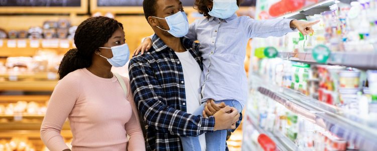 Family shopping during coronavirus pandemic. African American family with child wearing face masks, purchasing food at supermarket, panorama. Black parents with their kid buying products at mall