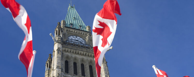 The Parliament of Canada's Peace Tower stands in front of a clear blue sky with Canadian flags blowing in the wind.