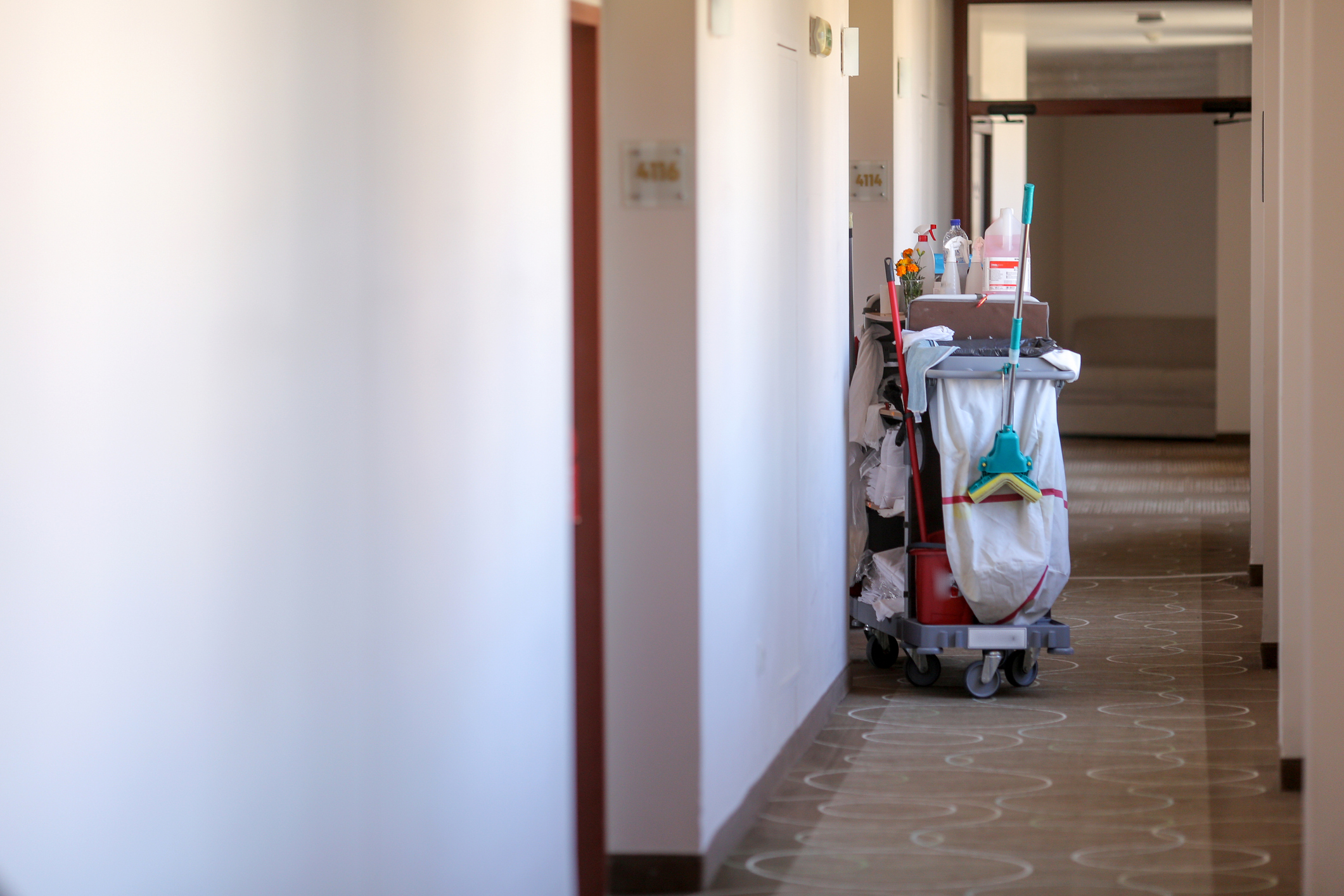 Photograph of a full hotel cleaner's cart in the empty hallway of a hotel.