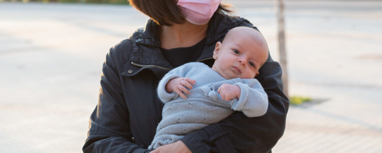Hispanic mother wearing a facemask outside and holding her baby, during the covid-19 pandemic
