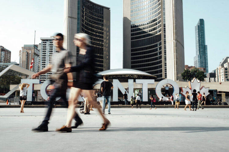 Two people walking in front of the Toronto sign downtown in front of City hall.