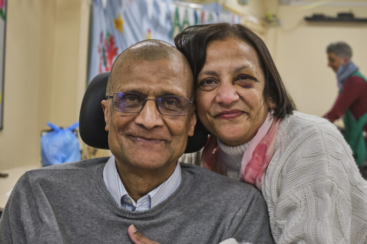 An older South Asian couple lean together and smile.