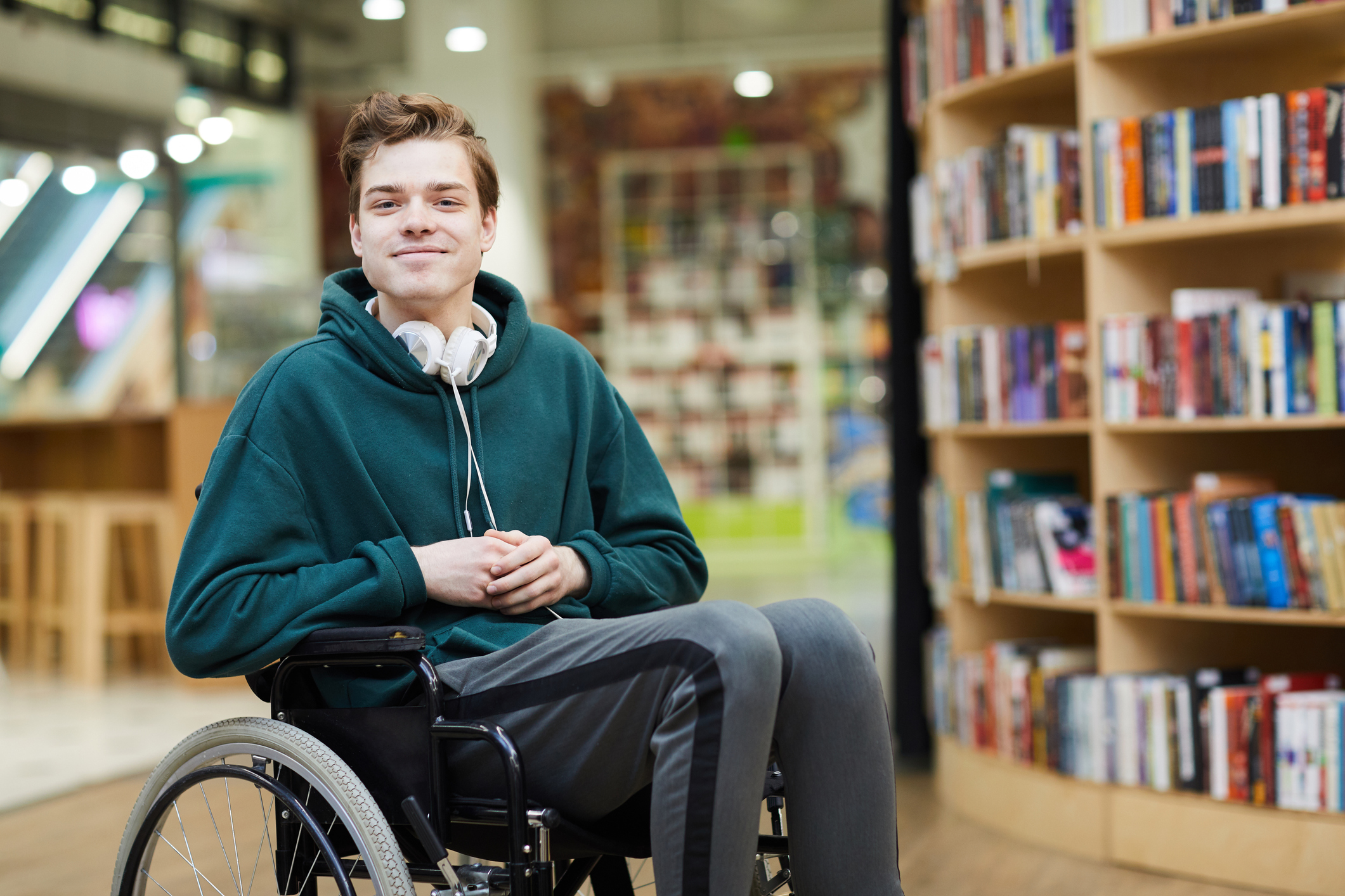 Image of a young man in a wheel chair with a library bookcase behind him.