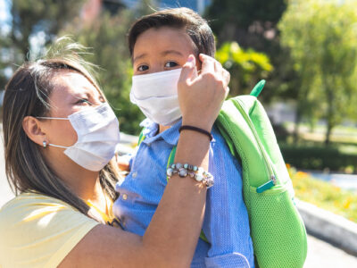 A Latin American mother holding her preschool son with a mask in a park