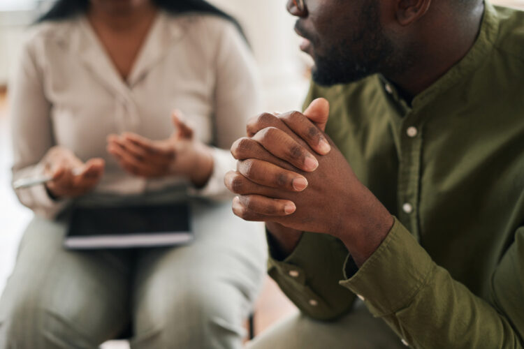 Image of a young, Black man's hands whose fingers are interlocked, sharing his concerns with counselor or psychotherapist while attending psychological session